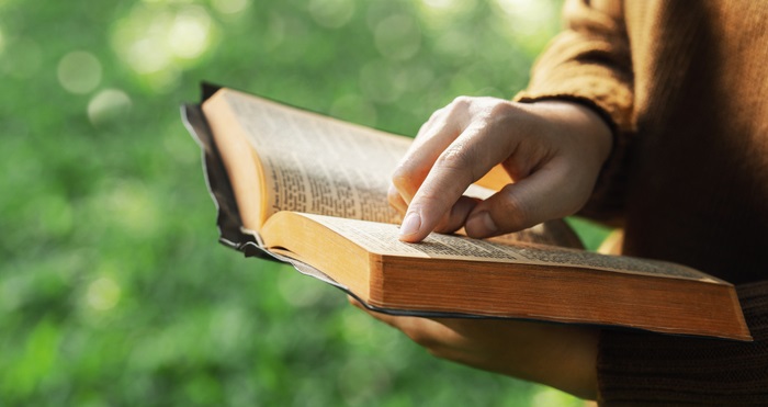 The concept of reading the Bible and praying for God&#8217;s blessings. Therapeutic living in peace with nature while spending time with God. Young woman&#8217;s hand pointing to a Bible topic