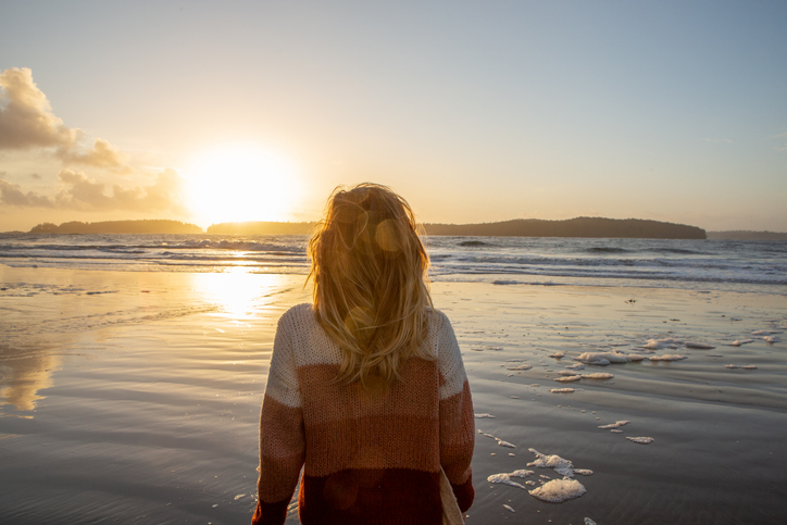 Young woman standing on beach at sunset watching the waves, wilderness area